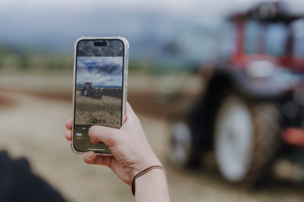 Ein Traktor am Feld der durch ein Handy fotografiert wird